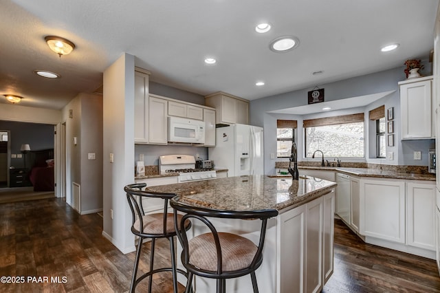 kitchen with a kitchen breakfast bar, white appliances, a center island, dark stone countertops, and dark wood-type flooring