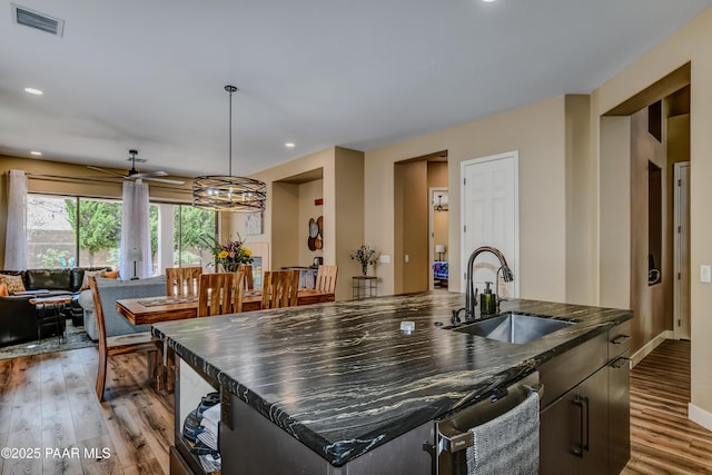 kitchen featuring a sink, a kitchen island with sink, light wood-style floors, dishwasher, and a ceiling fan