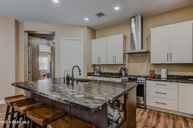 kitchen featuring stainless steel gas range, wall chimney exhaust hood, a sink, light wood-style flooring, and a breakfast bar area