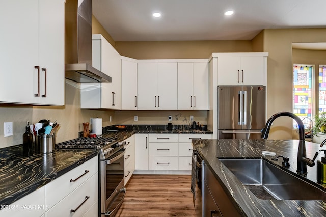 kitchen with stainless steel appliances, a sink, wall chimney range hood, wood finished floors, and recessed lighting