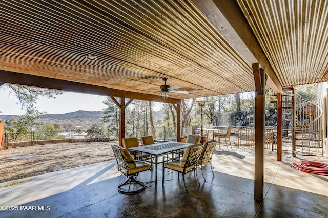 view of patio with stairway, a trampoline, fence, outdoor dining area, and a mountain view