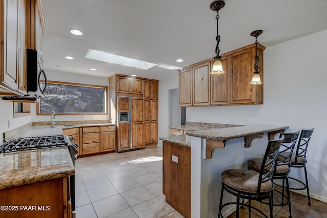 kitchen featuring a skylight, a breakfast bar area, light stone countertops, paneled refrigerator, and a peninsula