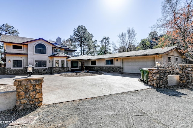 view of front of home with an attached garage, driveway, stone siding, stucco siding, and a chimney