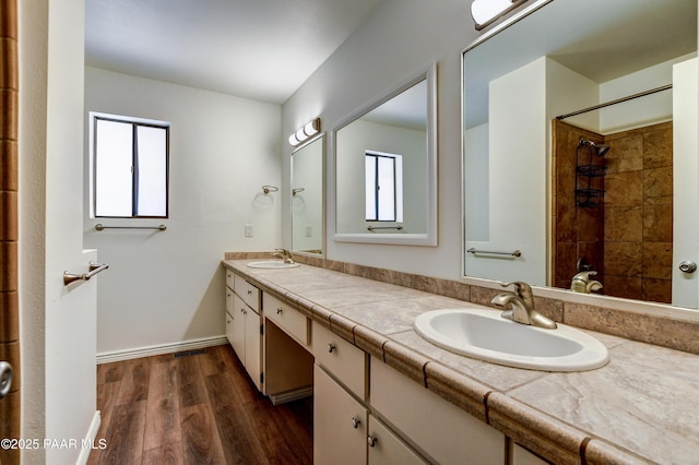 bathroom with double vanity, tiled shower, a sink, and wood finished floors