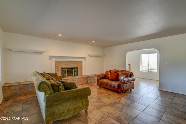 living area featuring arched walkways, recessed lighting, a stone fireplace, tile patterned flooring, and baseboards