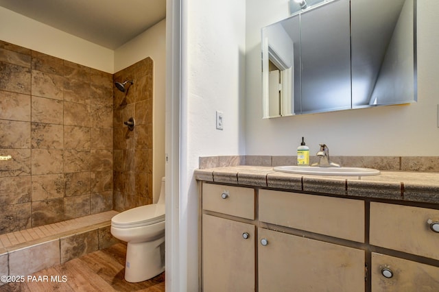 bathroom with toilet, vanity, wood finished floors, and tiled shower