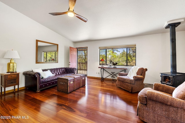 living area with a wood stove, wood finished floors, lofted ceiling, baseboards, and a ceiling fan