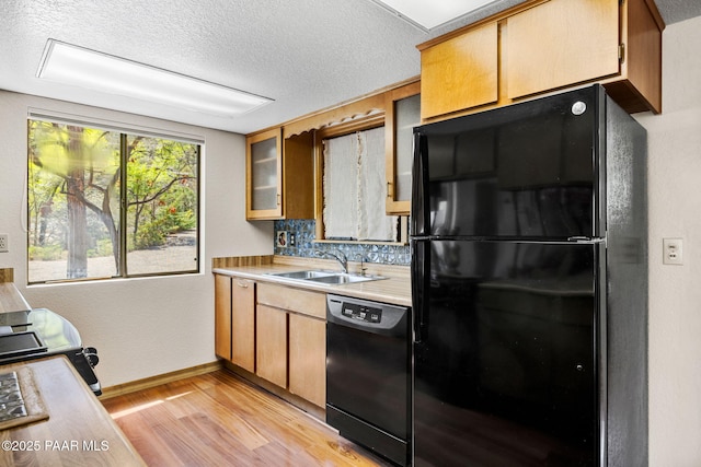 kitchen featuring a sink, light countertops, baseboards, black appliances, and light wood-style floors