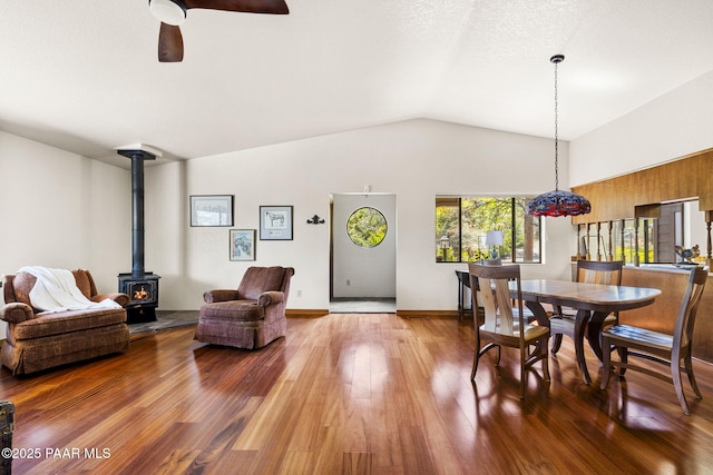 dining room with vaulted ceiling, ceiling fan, a wood stove, and wood finished floors
