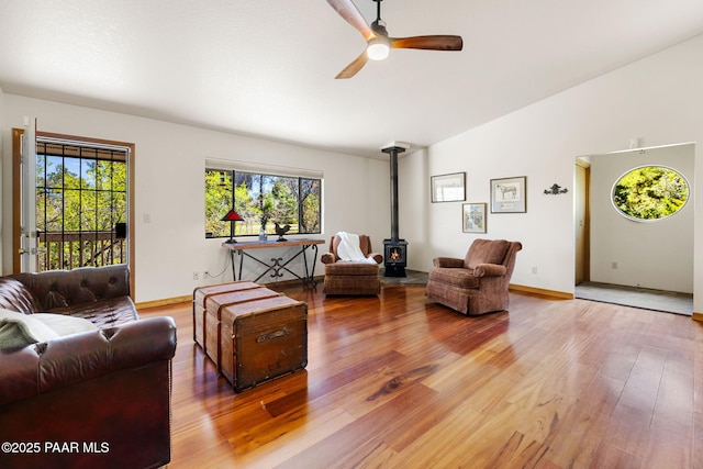 living room featuring a wood stove, light wood-style floors, baseboards, a ceiling fan, and vaulted ceiling
