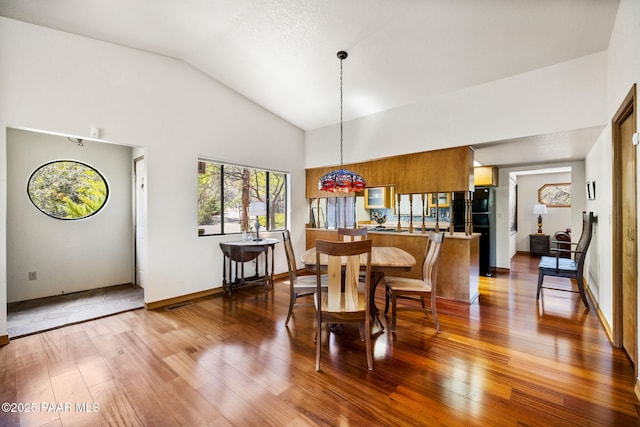 dining area featuring high vaulted ceiling, baseboards, and wood finished floors