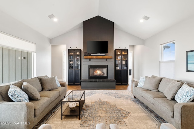 living area with high vaulted ceiling, a large fireplace, wood finished floors, visible vents, and baseboards