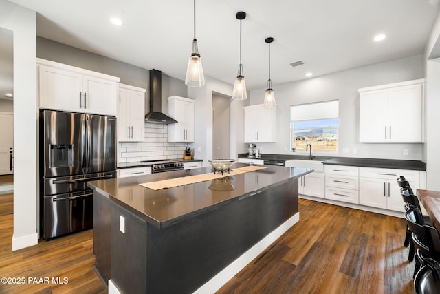 kitchen with dark wood-style floors, a center island, stainless steel appliances, dark countertops, and wall chimney exhaust hood