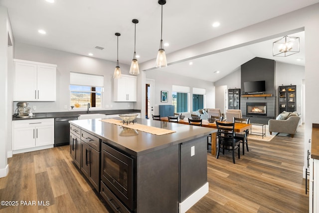 kitchen with stainless steel dishwasher, dark countertops, a fireplace, and white cabinetry