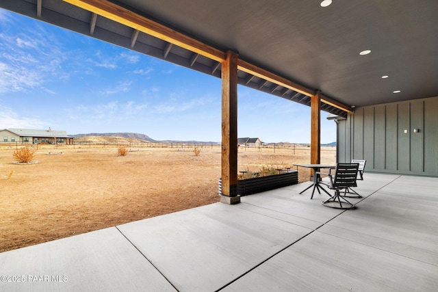 view of patio with outdoor dining space, fence, a mountain view, and a rural view