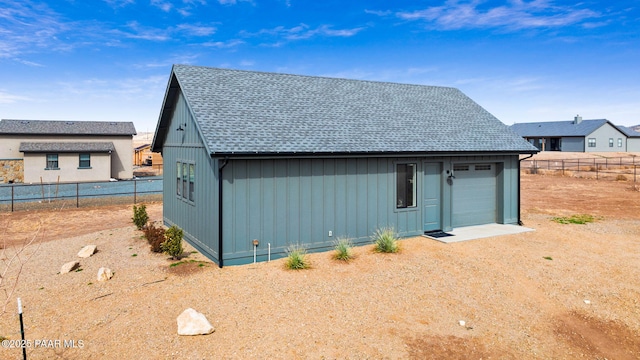 exterior space featuring roof with shingles, a detached garage, fence, driveway, and an outdoor structure