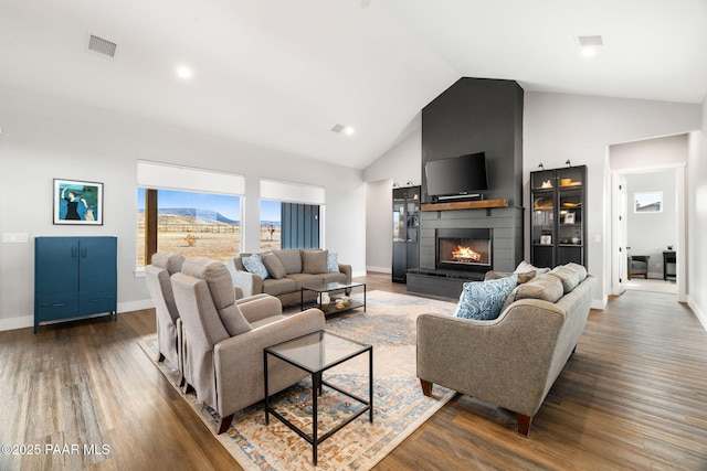 living room featuring a large fireplace, baseboards, visible vents, wood finished floors, and high vaulted ceiling