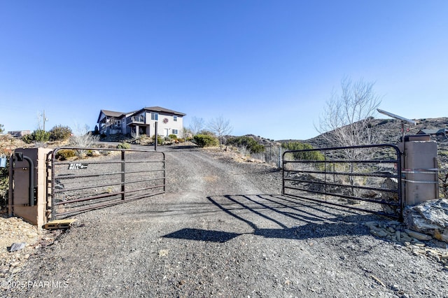 view of street with dirt driveway, a gated entry, and a gate