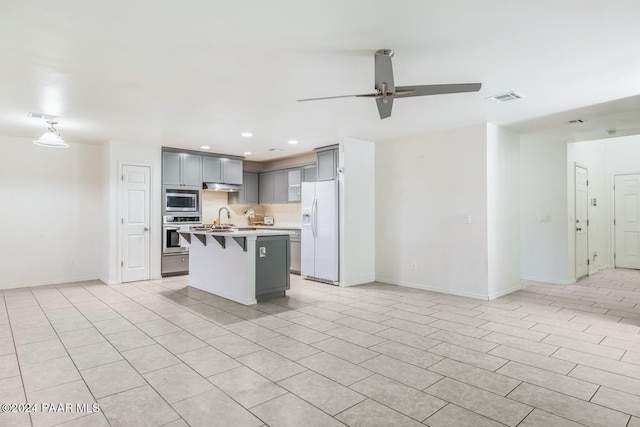 kitchen with gray cabinetry, stainless steel appliances, ceiling fan, a breakfast bar area, and an island with sink