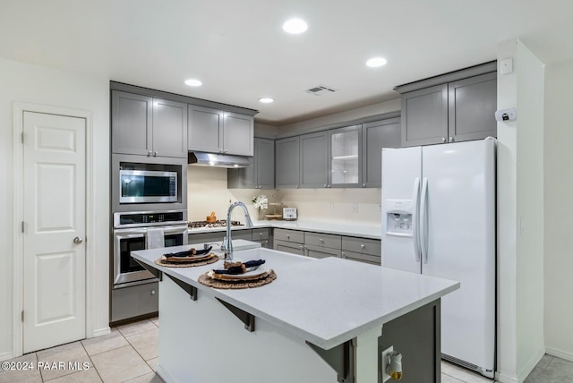 kitchen with appliances with stainless steel finishes, light tile patterned floors, a kitchen island with sink, and sink