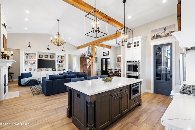 kitchen with beamed ceiling, stainless steel double oven, an inviting chandelier, light wood finished floors, and built in microwave