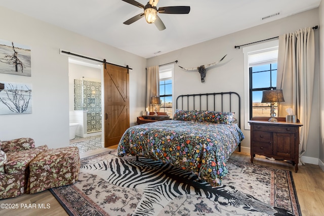 bedroom featuring a barn door, multiple windows, wood finished floors, and visible vents