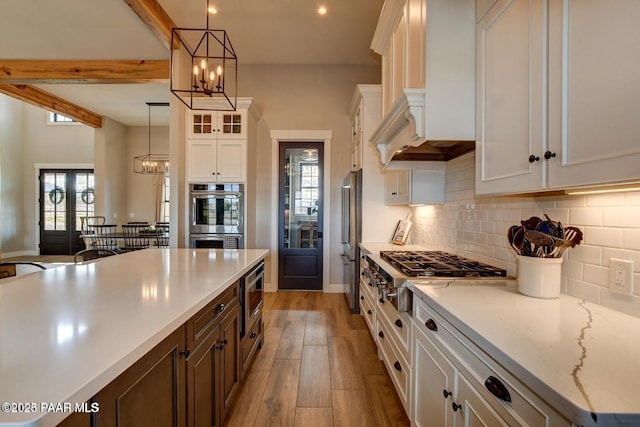 kitchen featuring light wood-type flooring, appliances with stainless steel finishes, white cabinetry, a notable chandelier, and tasteful backsplash