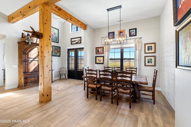 dining room with beam ceiling, french doors, light wood-type flooring, and a towering ceiling