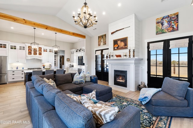 living room with a glass covered fireplace, light wood-style flooring, a notable chandelier, and french doors