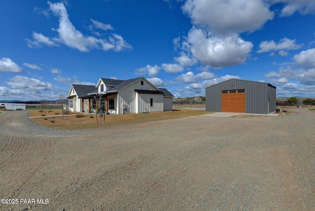 view of front facade featuring a detached garage, an outbuilding, and dirt driveway