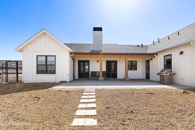 back of house with a shingled roof, a patio area, board and batten siding, and a chimney