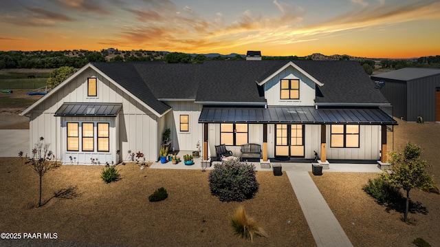 back of property at dusk featuring a standing seam roof, covered porch, board and batten siding, a shingled roof, and metal roof