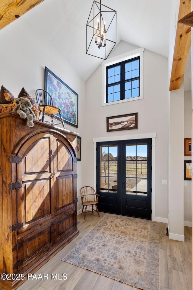 foyer with a chandelier, high vaulted ceiling, a wealth of natural light, and wood finished floors