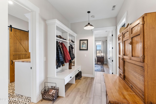 mudroom with light wood-type flooring, visible vents, a barn door, and baseboards