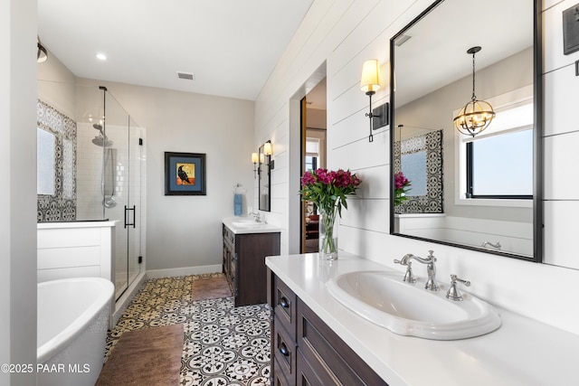 full bath with visible vents, a shower stall, two vanities, and a sink