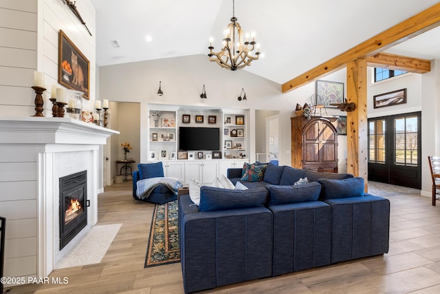 living area with high vaulted ceiling, a fireplace with flush hearth, beamed ceiling, light wood-type flooring, and a chandelier