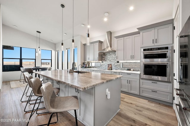 5692 E Cannon Pl, Prescott Valley, AZ 86314 - kitchen with wall chimney range hood, gray cabinetry, appliances with stainless steel finishes, decorative backsplash, and a kitchen island with sink