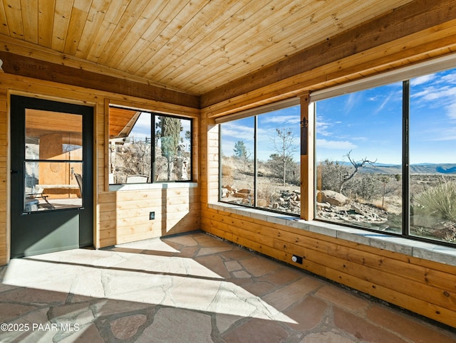 unfurnished sunroom featuring a healthy amount of sunlight, wood ceiling, and a mountain view