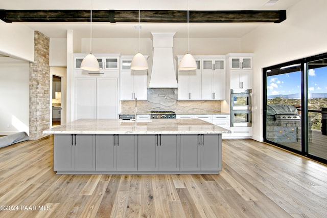 kitchen featuring a center island with sink, white cabinets, and custom range hood