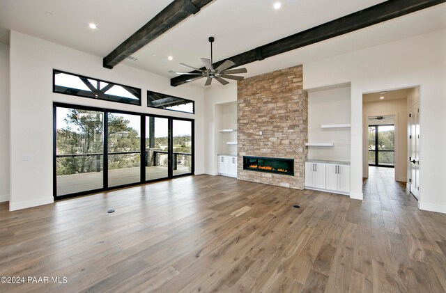 unfurnished living room featuring beamed ceiling, light wood-type flooring, a stone fireplace, and a wealth of natural light