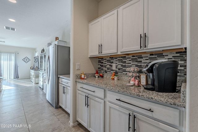 kitchen featuring light tile patterned floors, tasteful backsplash, light stone countertops, white cabinets, and stainless steel refrigerator