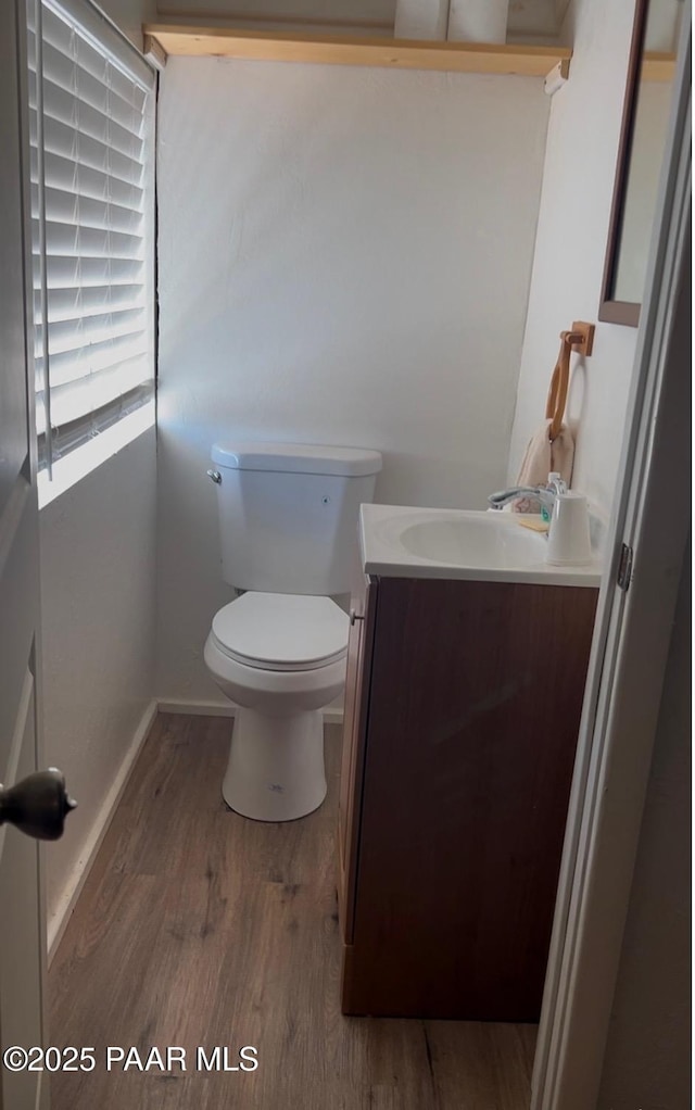 half bath with baseboards, toilet, wood finished floors, and vanity