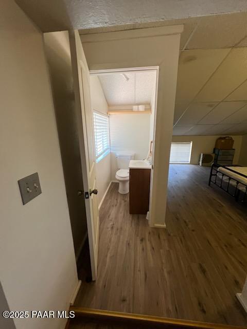 half bathroom featuring vaulted ceiling, toilet, wood finished floors, and baseboards