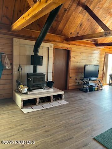 living room with beam ceiling, wooden walls, wood ceiling, and a wood stove