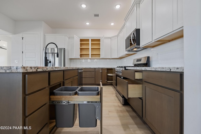 kitchen featuring light stone countertops, backsplash, light hardwood / wood-style floors, white cabinets, and appliances with stainless steel finishes