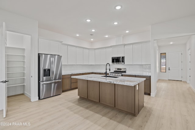 kitchen with light stone countertops, appliances with stainless steel finishes, a center island with sink, light hardwood / wood-style floors, and white cabinetry