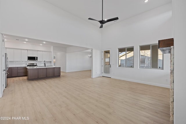 unfurnished living room with light wood-type flooring, high vaulted ceiling, ceiling fan, and sink