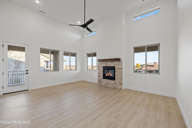 unfurnished living room with ceiling fan, a stone fireplace, light wood-type flooring, and a high ceiling