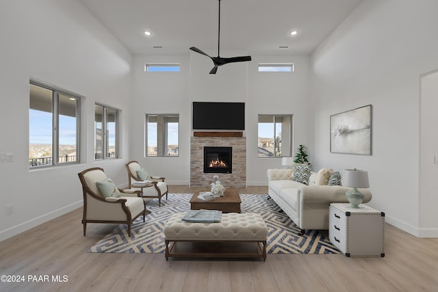 living room featuring a stone fireplace, a high ceiling, and light wood-type flooring