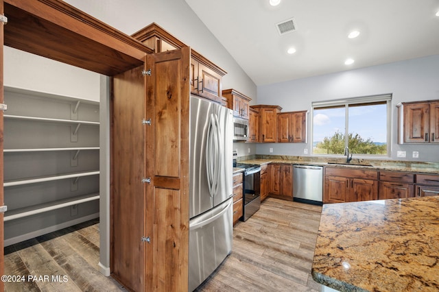 kitchen featuring light stone countertops, stainless steel appliances, vaulted ceiling, and light hardwood / wood-style floors